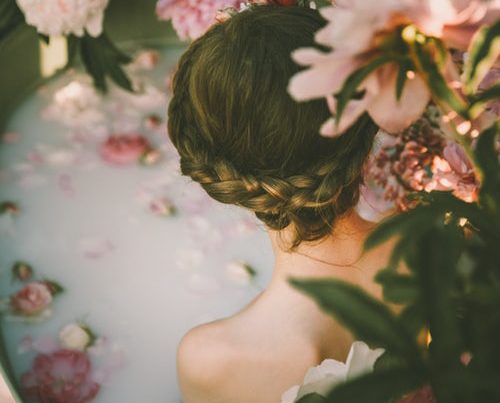 A ritual bath consisting of pink peonies and milk surrounding a girl with braided hair