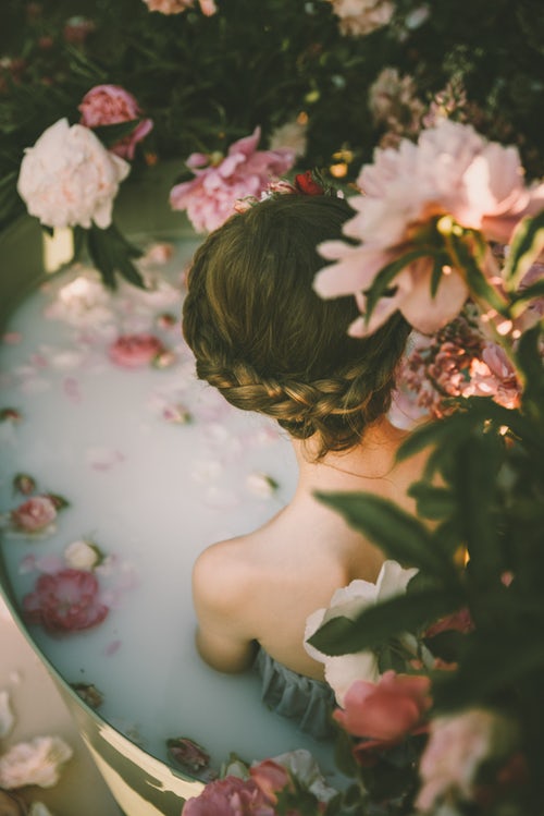 A ritual bath consisting of pink peonies and milk surrounding a girl with braided hair