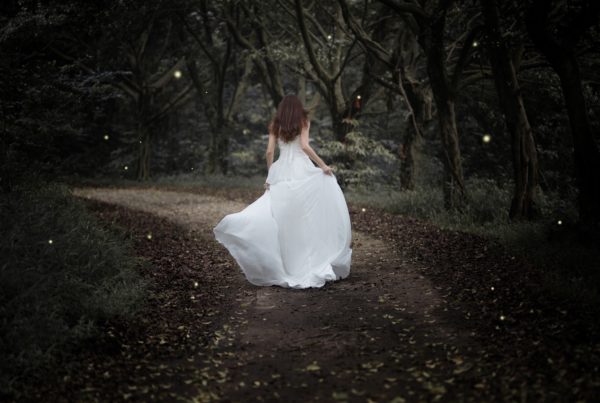 girl in white gown running down forest path