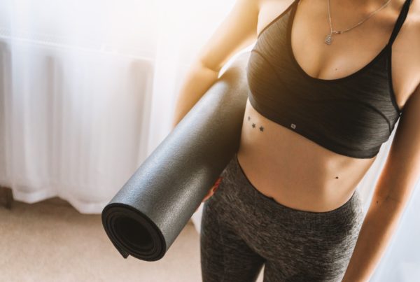 Photo of a woman in a sports bra and leggings holding a yoga mat