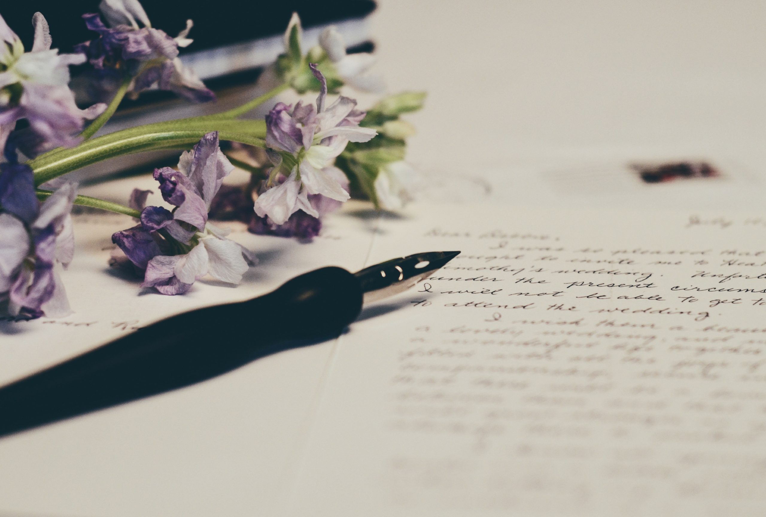 A quill and lavender flowers sitting on type of a cursive handwritten letter