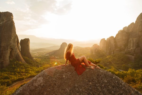 A blonde in a red dress sitting on top of a tall rock