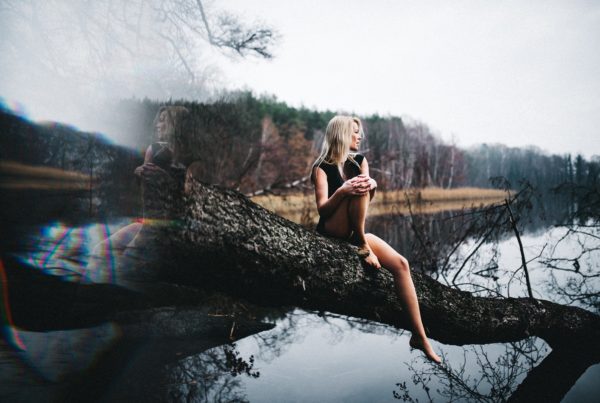 Girl sitting in a log over the river; image is reflected