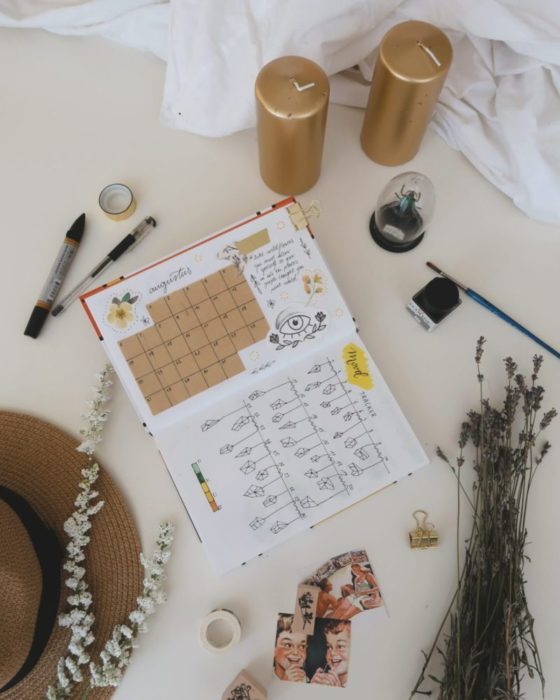 A calendar/journal surrounded by various writing implements, candles, a hat, lavender