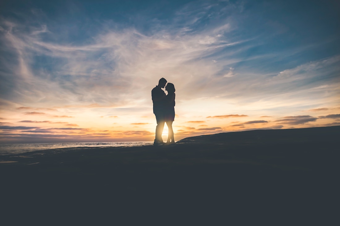 a couple standing close near a beach during sunset