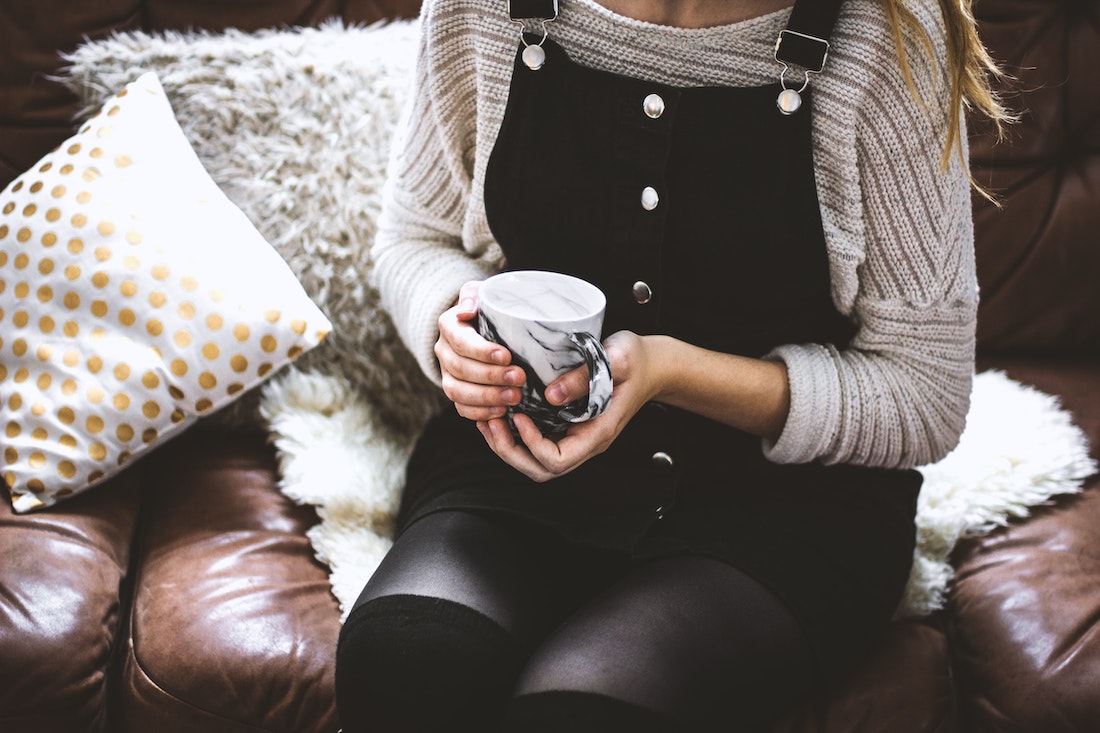 woman wearing a sweater, drinking a hot beverage on a cozy couch