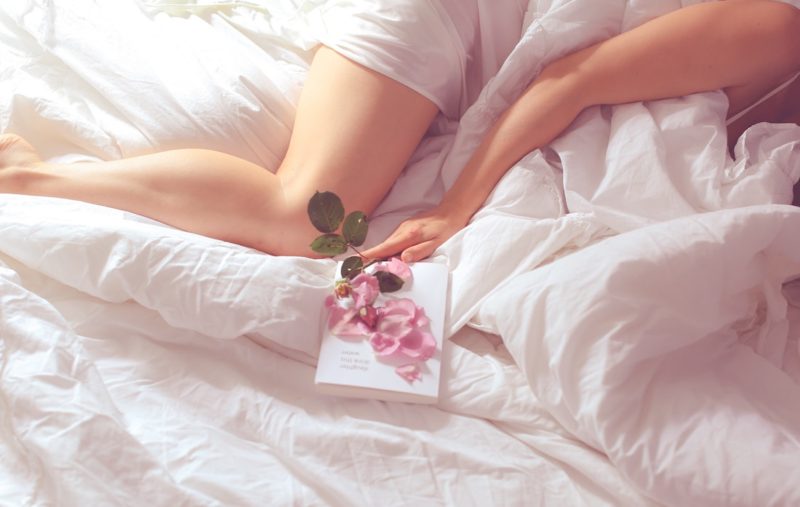woman in bed with a book and pink rose petals