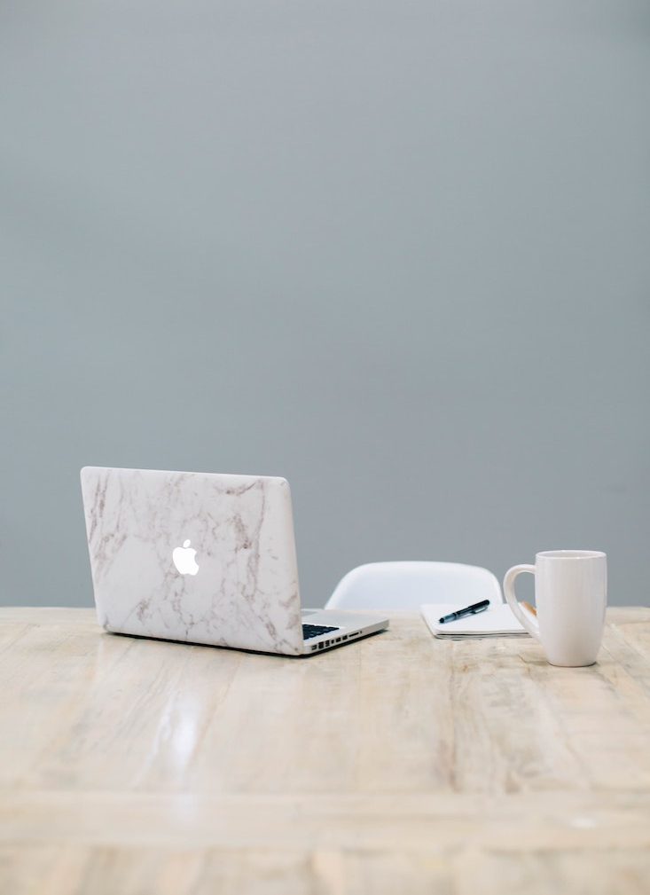 an elegant desk with a computer, journal and mug