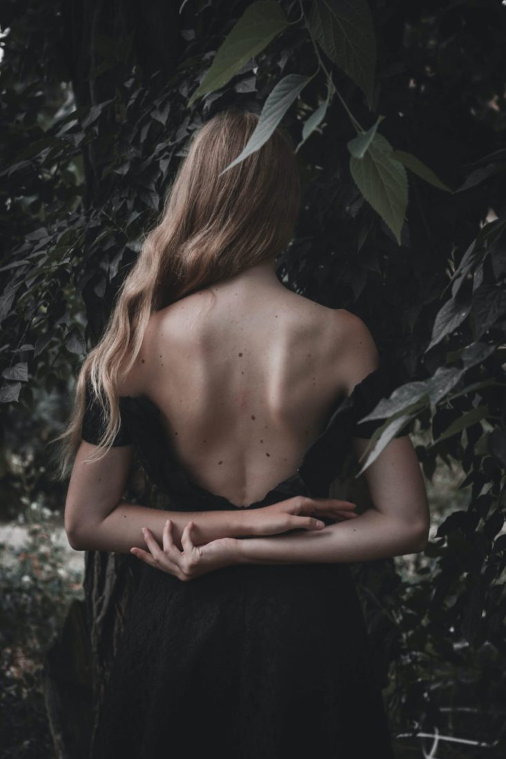 woman holding her arms behind her back wearing a black dress in the foliage