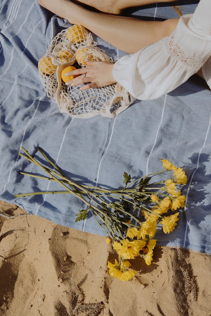 woman sitting on a beach towel with yellow flowers and lemons